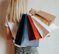 Woman holding colorful shopping bags against a wall.
